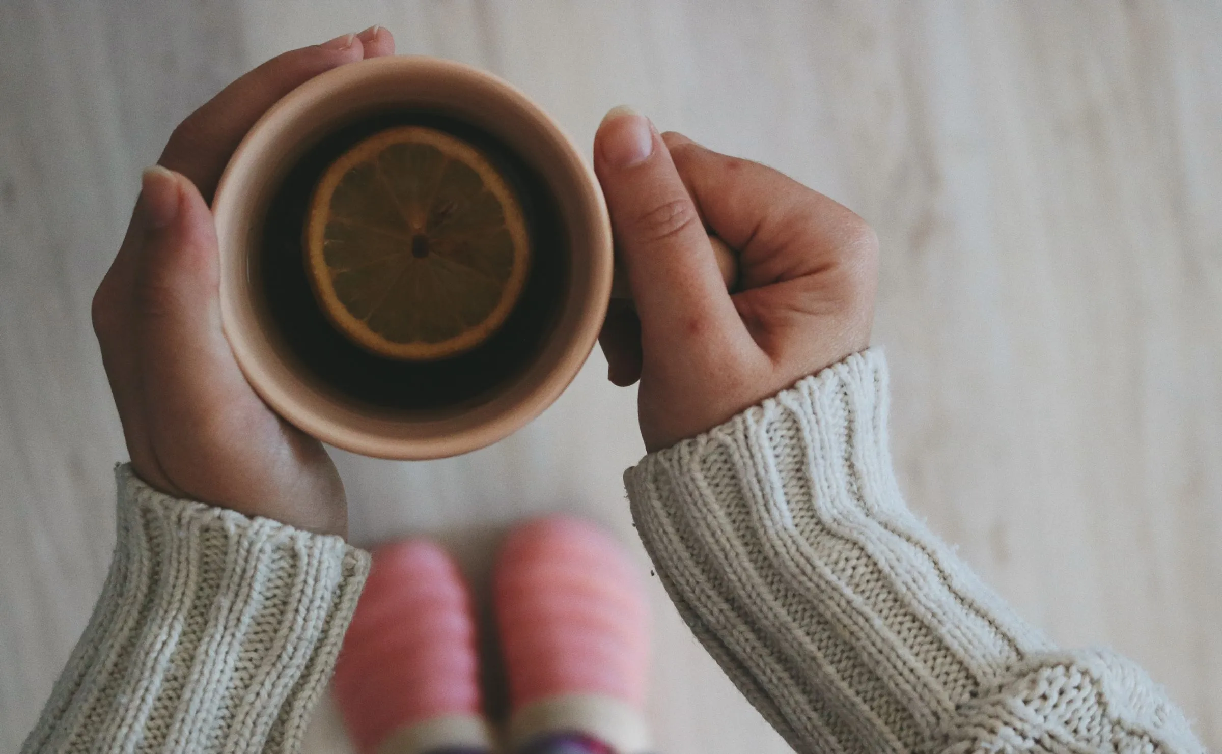 Two hands in a soft knitted sweater holding a mug of lemon tea.